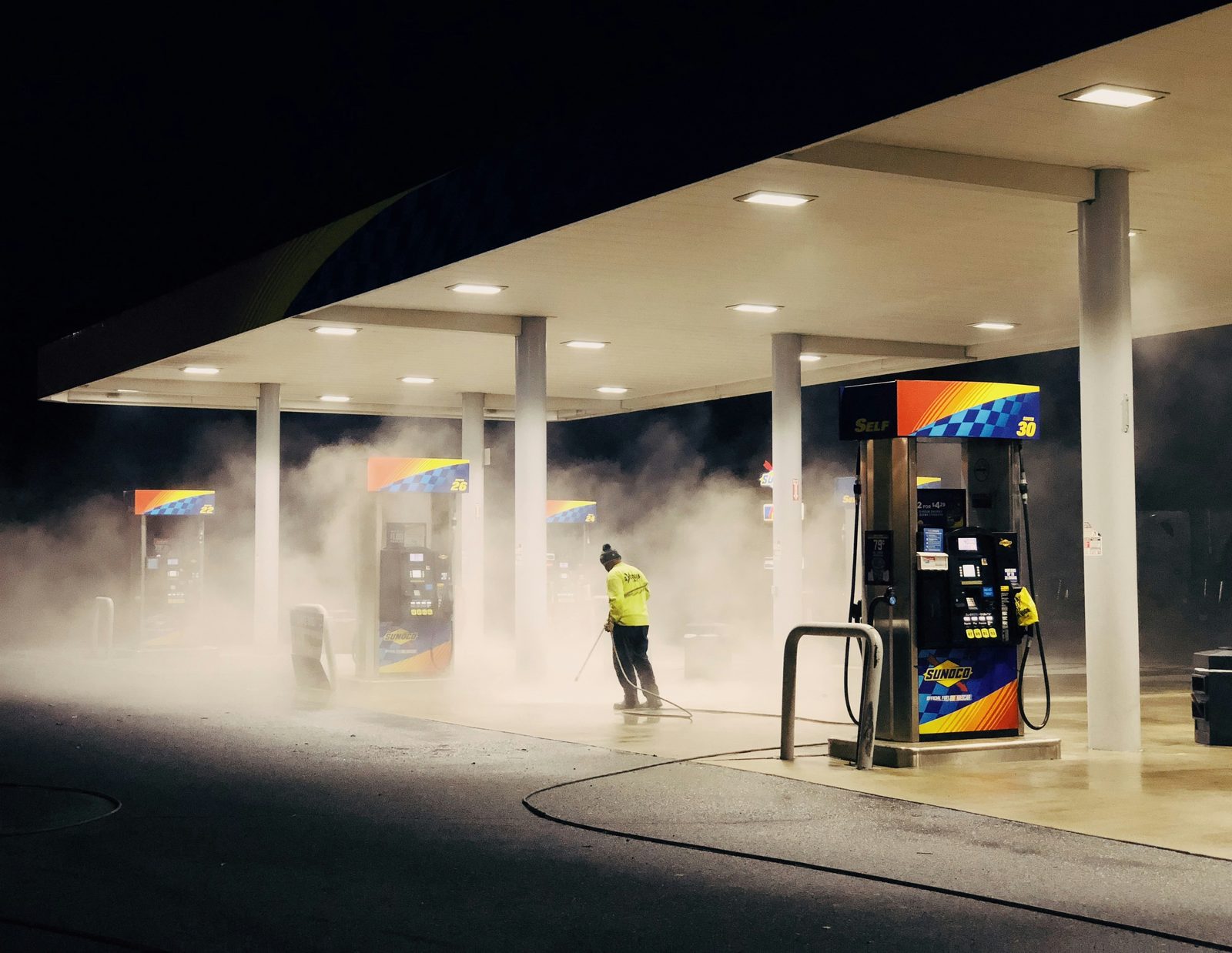 Hot water pressure washing of a gas station forecourt and fuel pump island at night