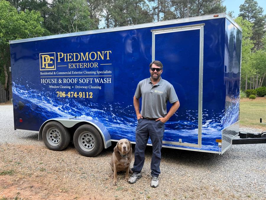 Trey Claus, owner of Piedmont Exterior LLC, with his dog in front of the branded trailer in Madison, GA